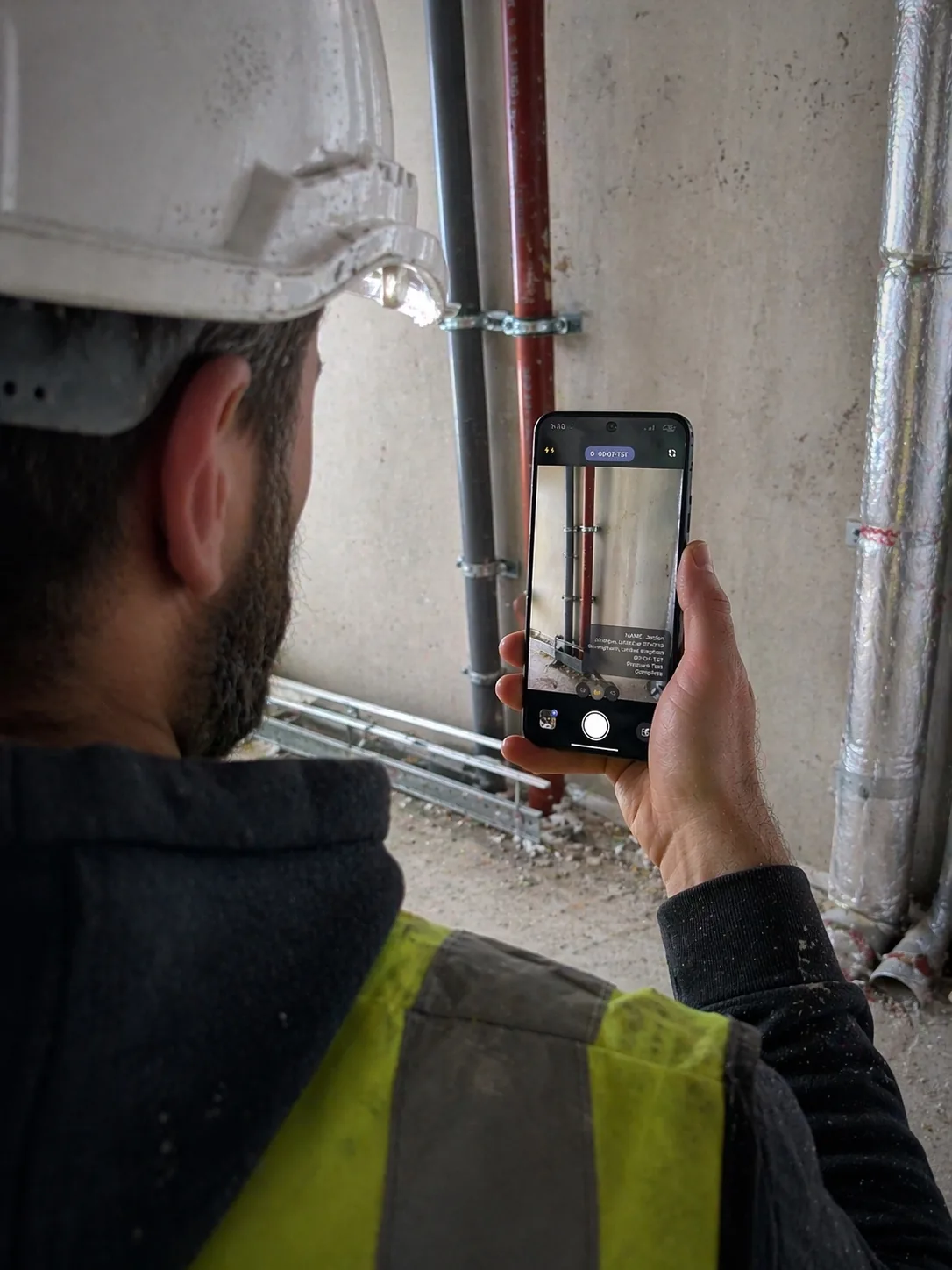 Construction worker using the BuildIntel Camera app to photograph pipework testing on a live site